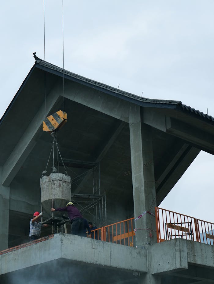 Workers operate a crane lifting concrete on a building under construction, showcasing construction industry dynamics.